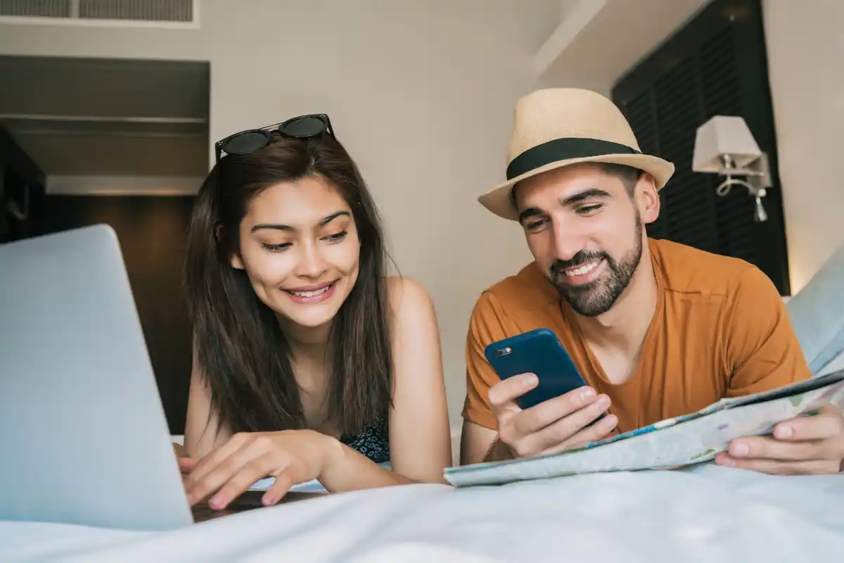 dutch couple booking hotel on phone and laptop at home