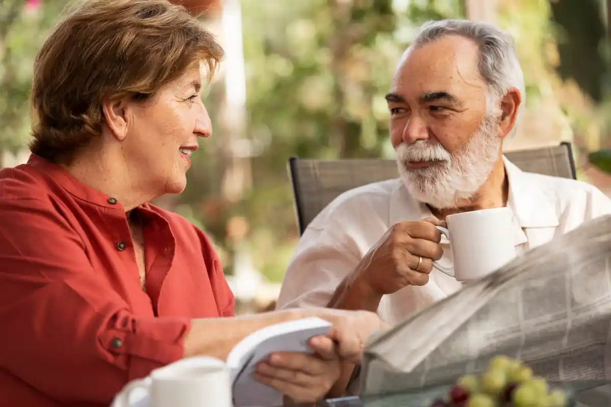 two older Dutch people laughing together at home with coffee