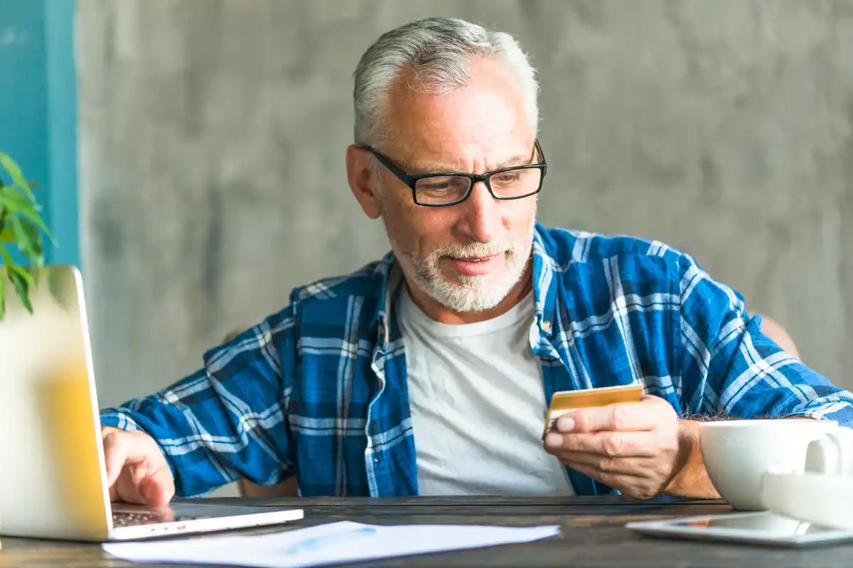 Dutch elderly person comparing household bills with laptop and coffee